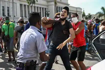 Una fotografía de las protestas del 11 de julio de 2021 en Cuba, que muestra un caso de represión estatal. Un joven está siendo detenido por un oficial de seguridad en una bulliciosa calle, lo que indica la agitación civil que generó discusiones internacionales sobre Cuba en el CDH de la ONU.