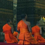 Buddhist monks in vibrant orange robes meditate in a richly decorated temple, symbolizing the essence of religious freedom.