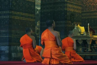 Buddhist monks in vibrant orange robes meditate in a richly decorated temple, symbolizing the essence of religious freedom.