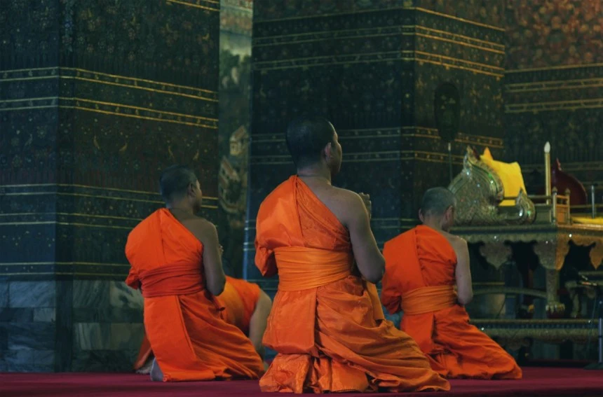 Buddhist monks in vibrant orange robes meditate in a richly decorated temple, symbolizing the essence of religious freedom.