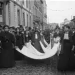 Fotografía histórica en blanco y negro capturando un momento de las revoluciones de principios del siglo XX, mostrando un grupo de mujeres, probablemente estudiantes de la Escola Normal de Lisboa, participando en un evento benéfico para las víctimas de la Revolución Republicana Portuguesa de 1910.