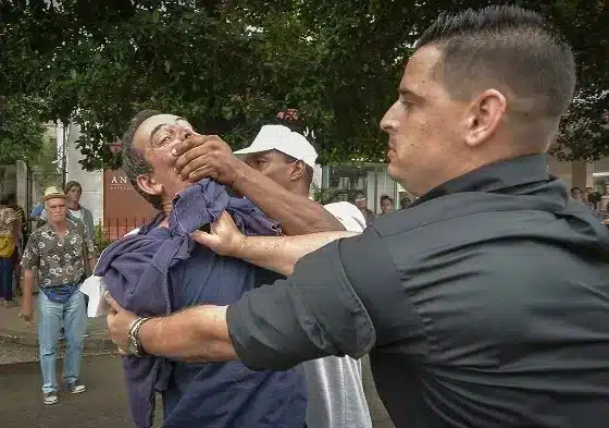 An officer detains Cuban journalist Lázaro Yuri Valle Roca during a 2019 protest, epitomizing the repression under the totalitarian Cuban regime and the ongoing struggle for press freedom.