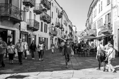 A bustling street scene in Aosta, representing the vibrant social tapestry where linguistic diversity thrives. People from various walks of life engage in daily activities, potentially conversing in a multitude of languages and dialects that echo the region's rich cultural heritage