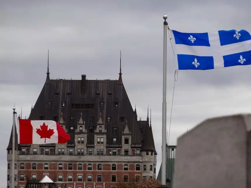 Banderas de Canadá y Quebec ondeando frente al Château Frontenac bajo un cielo nublado, simbolizando el federalismo multinacional en la Ciudad de Quebec, donde coexisten identidades culturales distintas dentro de la federación canadiense.