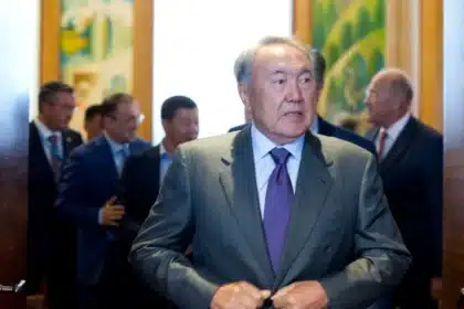 Former President Nursultan Nazarbayev of Kazakhstan walking through a hallway surrounded by other officials, symbolizing the authority he wielded, in a context where autocratic elections have been a subject of international scrutiny.