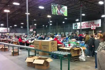 Volunteers participate in 'Operation Christmas Child', a manifestation of Christian globalism, at a large warehouse. They are busy packing donation boxes intended for children globally, reflecting the charitable spirit and community engagement of the holiday season.