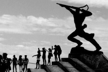 The New Man statue in Durres, Albania, stands as a silhouette against the sky, symbolizing strength and forward-looking determination, while a group of lively people mirror its stance, celebrating the spirit of unity and progress.