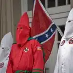 Miembros de un grupo supremacista blanco, vestidos con capuchas y túnicas icónicas, marchan llevando la bandera Confederada – una ofensa profunda y símbolo de intolerancia racial, provocando un choque entre los ideales de libertad de expresión y la protección de la dignidad según las discusiones sobre los límites de la tolerancia y la libertad.