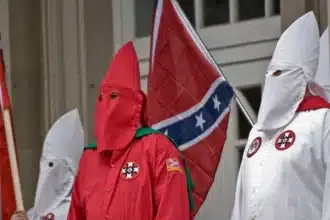 Members of a white supremacist group, clad in iconic hoods and robes, march bearing the Confederate flag – a profound offense and symbol of racial intolerance, igniting a clash between the ideals of freedom of expression and the protection of dignity as per the discussions on the boundaries of tolerance and liberty.