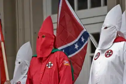 Miembros de un grupo supremacista blanco, vestidos con capuchas y túnicas icónicas, marchan llevando la bandera Confederada – una ofensa profunda y símbolo de intolerancia racial, provocando un choque entre los ideales de libertad de expresión y la protección de la dignidad según las discusiones sobre los límites de la tolerancia y la libertad.