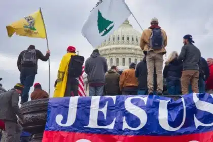 Un groupe d'individus avec des drapeaux et des bannières, mettant en avant le nom de «JÉSUS», se tenant devant un bâtiment important qui semble être le Capitole des États-Unis. Cette scène pourrait être associée aux événements du 6 janvier 2021, où l'intersection de l'activisme politique, du ferveur religieux et du sentiment nationaliste étaient visiblement exposés. La présence de symbolisme religieux, comme la bannière «JÉSUS», suggère l'implication de certains groupes qui peuvent mélanger leurs vues politiques avec leurs croyances religieuses, ce qui s'aligne avec des idéologies comme celles propagées par le mouvement Identité Chrétienne.
