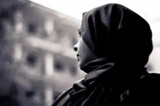 The image portrays a moment of quiet reflection, capturing a Muslim woman in profile, her gaze directed towards an unseen horizon. This evocative black and white photograph symbolizes the complexities of multiculturalism in France, emphasizing the experiences and challenges faced by Muslim women within a diverse society.