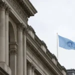 Drapeau des Nations Unies flottant au-dessus d'un bâtiment à l'architecture classique, représentant la gouvernance mondiale et la Démocratie Cosmopolite.