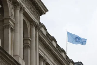 Bandera de las Naciones Unidas ondeando sobre un edificio de arquitectura clásica, representando la gobernanza global y la Democracia Cosmopolita.