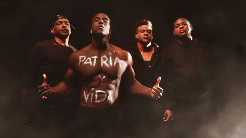 Four men stand together, with one in the center displaying the words "Patria y Vida" written across his bare chest. The image evokes the spirit of the song "Patria y Vida," which has become an anthem of resistance against the Cuban dictatorship. Their serious expressions and dark clothing underline the song's powerful message and the unity of Cubans in their fight for freedom and justice.