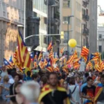 Una gran multitud de personas participando en una protesta por la independencia de Cataluña, marchando por las calles de la ciudad y ondeando numerosas banderas catalanas, abogando por los derechos políticos y la independencia de España.