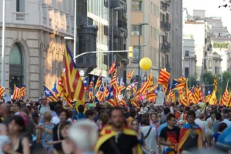 Una gran multitud de personas participando en una protesta por la independencia de Cataluña, marchando por las calles de la ciudad y ondeando numerosas banderas catalanas, abogando por los derechos políticos y la independencia de España.