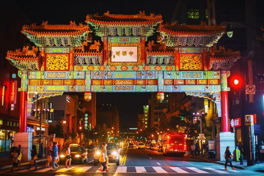 Night view of the vibrant, colorfully lit Friendship Archway in Chinatown, Washington DC, symbolizing People's Diplomacy, bustling with pedestrians and cars.