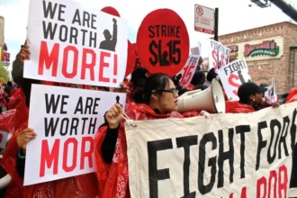 <p>Un grupo de manifestantes sostiene carteles y pancartas durante una manifestación por salarios justos. Los carteles dicen "¡VALORAMOS MÁS!", "HUELGA $15" y "LUCHA POR $15". Están abogando por un aumento del salario mínimo a $15 por hora. Esta imagen captura su llamado colectivo por el reconocimiento de su valor y la necesidad de una compensación justa en el lugar de trabajo. Foto de Bob Simpson (CC BY-NC-SA)</p>