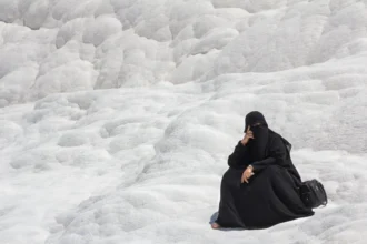 En la imagen, una mujer con una burka negra está sentada sobre una superficie rocosa y blanca. Este contraste visual resalta las tensiones entre las tradiciones religiosas y el concepto de laicismo, que busca la separación entre religión y estado, promoviendo una sociedad donde las creencias individuales no interfieran con la gobernanza pública o los derechos civiles.