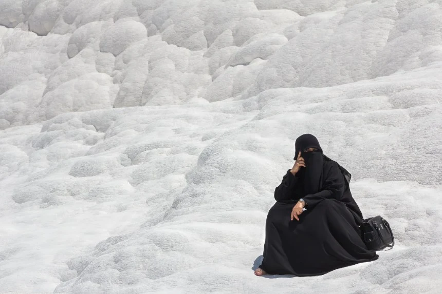 In the image, a woman wearing a black burqa is sitting on a white, rocky surface. This visual contrast highlights the tensions between religious traditions and the concept of secularism, which seeks the separation of religion and state, promoting a society where individual beliefs do not interfere with public governance or civil rights.
