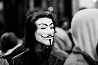 Person wearing a Guy Fawkes mask, a popular symbol of the fight against censorship, in an urban setting. The mask represents resistance against oppression and the tyranny of prevailing opinion.