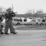 El 7 de marzo de 1965, 600 manifestantes por los derechos civiles liderados por Hosea Williams (al frente derecho con abrigo oscuro) y John Lewis (a la derecha con abrigo de color claro) cruzaron el puente Edmund Pettus en Selma, Alabama. Fueron recibidos por policías estatales y locales, quienes les dieron una advertencia de dos minutos para dispersarse. Cuando los manifestantes se negaron, los oficiales los atacaron con gases lacrimógenos y los golpearon, resultando en más de 50 hospitalizaciones. Archivo de Fotos GPA (CC BY-NC).