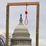 Democracia militante: Imagen de una horca de madera improvisada con una soga, con el edificio del Capitolio de los Estados Unidos en el fondo. Esta escena es del ataque al Capitolio el 6 de enero de 2021.