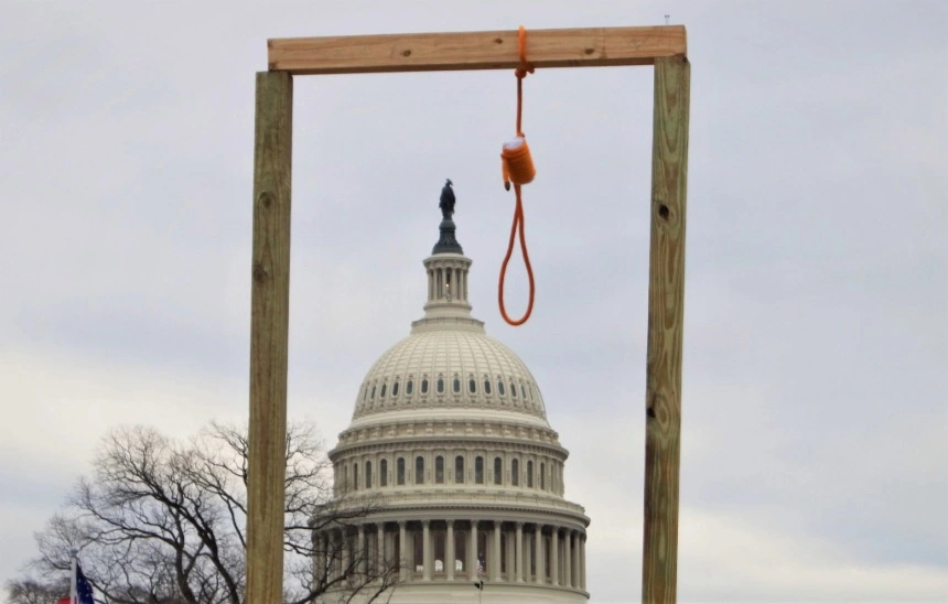 Democracia militante: Imagen de una horca de madera improvisada con una soga, con el edificio del Capitolio de los Estados Unidos en el fondo. Esta escena es del ataque al Capitolio el 6 de enero de 2021.