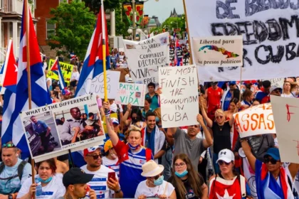 Una multitud de manifestantes cubanos en Canadá se ha reunido para protestar contra la dictadura en Cuba. Los manifestantes sostienen carteles expresando su rechazo al régimen comunista y denunciando los asesinatos y la opresión política. Algunos de los carteles visibles en la imagen incluyen mensajes como "Libertad para los presos políticos", "Patria y Vida", "Viva Cuba libre" y "We must finish the communism in Cuba". La protesta resalta la demanda de libertad y derechos humanos para los cubanos, así como la condena a la represión y violaciones de derechos humanos por parte del gobierno cubano. Además, se pueden ver banderas cubanas y varias imágenes que contrastan la situación en Cuba con otras realidades.
