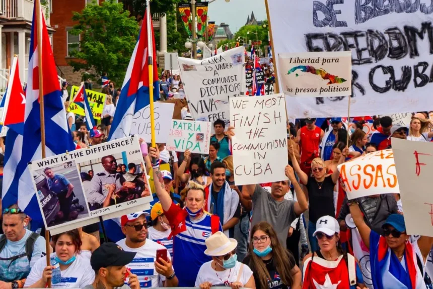 A crowd of Cuban protesters in Canada has gathered to protest against the dictatorship in Cuba. The demonstrators are holding signs expressing their rejection of the communist regime and denouncing the murders and political oppression. Some of the visible signs in the image include messages like "Libertad para los presos políticos" (Freedom for political prisoners), "Patria y Vida" (Homeland and Life), "Viva Cuba libre" (Long live free Cuba), and "We must finish the communism in Cuba." The protest highlights the demand for freedom and human rights for Cubans, as well as the condemnation of the repression and human rights violations by the Cuban government. Additionally, Cuban flags and various images contrasting the situation in Cuba with other realities can be seen.