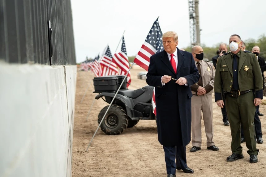 L'image montre le président Donald Trump se préparant à signer une plaque le long du mur frontalier entre le Texas et le Mexique en janvier 2021. Cet acte symbolise l'idéologie nativiste, soulignant la protection de l'identité nationale par le renforcement des frontières et la justification de mesures strictes contre les étrangers perçus. Le mur frontalier lui-même est devenu un symbole clé du nativisme, reflétant les efforts pour maintenir une identité nationale homogène.