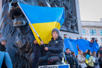 A young boy holds the Ukrainian flag during a demonstration, symbolizing resilience and national pride amidst the ongoing conflict. The crowd in the background showcases strong support for Ukraine.