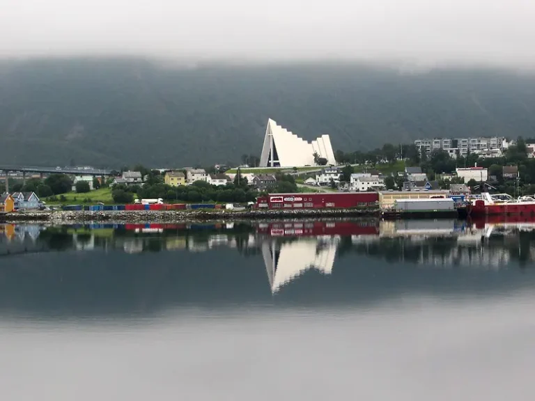 The Arctic Cathedral is prominently featured, reflecting in the waters of a Norwegian fjord, identifiable by its unique triangular structure.
