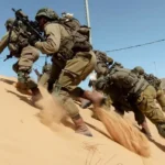 The image shows soldiers moving quickly up a sandy hill, appearing to be in a tactical operation. The uniforms suggest they belong to the Israel Defense Forces (IDF), aligning with ongoing tensions in the Israel-Iran conflict.