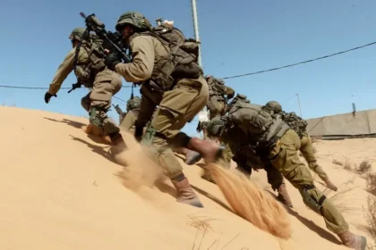 The image shows soldiers moving quickly up a sandy hill, appearing to be in a tactical operation. The uniforms suggest they belong to the Israel Defense Forces (IDF), aligning with ongoing tensions in the Israel-Iran conflict.