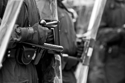 Primer plano de agentes de la policía antidisturbios sosteniendo porras y escudos, representando cuestiones relacionadas con la justicia penal y las prácticas de aplicación de la ley.