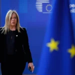 Giorgia Meloni, a prominent far-right political leader in Italy, walking past an EU flag during a European Council meeting. The image highlights the complex relationship between far-right parties and the European Union, as Meloni's party navigates its stance on European integration while holding nationalist views. The blurred EU flag in the foreground emphasizes the centrality of the EU in far-right political discourse.