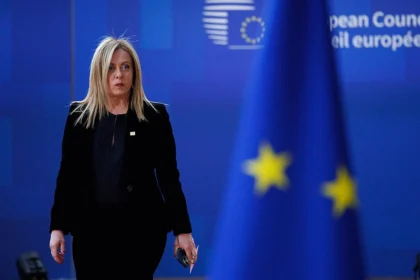 Giorgia Meloni, a prominent far-right political leader in Italy, walking past an EU flag during a European Council meeting. The image highlights the complex relationship between far-right parties and the European Union, as Meloni's party navigates its stance on European integration while holding nationalist views. The blurred EU flag in the foreground emphasizes the centrality of the EU in far-right political discourse.