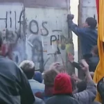 Multitud reunida en el Muro de Berlín mientras un hombre lo rompe con un martillo, simbolizando la atracción magnética del poder blando occidental. Este momento captura cómo los ideales de libertad y apertura atrajeron a personas del Este, mostrando la influencia del atractivo cultural e ideológico sobre la fuerza, un concepto central en el poder blando.