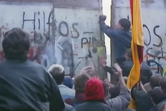 Multitud reunida en el Muro de Berlín mientras un hombre lo rompe con un martillo, simbolizando la atracción magnética del poder blando occidental. Este momento captura cómo los ideales de libertad y apertura atrajeron a personas del Este, mostrando la influencia del atractivo cultural e ideológico sobre la fuerza, un concepto central en el poder blando.