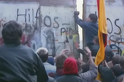 Crowd gathered at the Berlin Wall as a man breaks through with a hammer, symbolizing the magnetic pull of Western soft power. This moment captures how ideals of freedom and openness attracted people from the East, showcasing the influence of cultural and ideological appeal over force, a core concept in soft power.