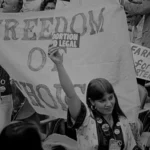 Abortion Pill: A Democratic delegate at the 1976 convention holds a sign advocating for abortion rights, with a backdrop of banners reading "Freedom of Choice." – Photo by Warren K. Leffler.
