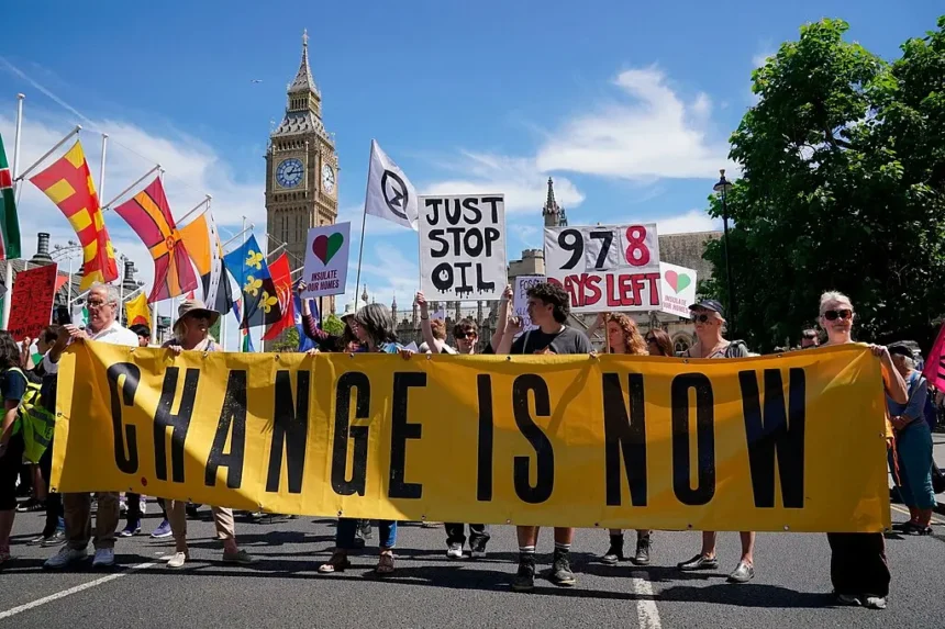 Une manifestation pour l'activisme climatique, avec des manifestants tenant des banderoles et des pancartes portant des messages tels que "Le changement, c'est maintenant" et "Just Stop Oil". Le cadre inclut des monuments emblématiques, suggérant la visibilité de la manifestation dans un centre public ou politique.