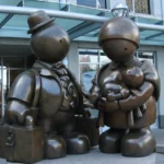 A bronze sculpture titled 'Immigrant Family' by Tom Otterness, symbolizing the challenges and journeys of immigrant families, placed outside a public building to inspire reflection on immigration policies.