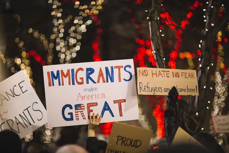 Demonstrators hold signs emphasizing the positive impact of immigrants and rejecting fear-driven narratives, highlighting the need for policies that align with inclusivity and national benefit.