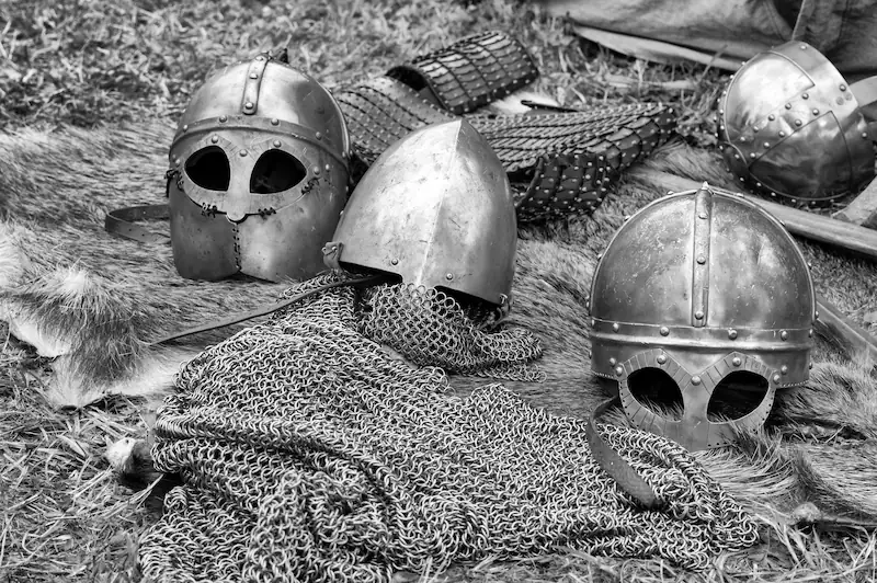 Black-and-white image of medieval helmets and chainmail armor laid on the ground, representing historical warfare and the underlying causes of war, including territorial conquest and resource competition.