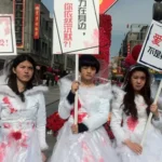 Mascarade numérique. Trois militantes féministes chinoises, habillées en mariées avec des taches rouges ressemblant à du sang, tiennent des pancartes de protestation contre les violences de genre dans une rue animée. Leurs expressions sont sérieuses et défiantes, symbolisant la résistance contre la censure et la répression de l’État. La scène représente une forme créative d’activisme féministe et queer en Chine.