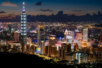 A nighttime aerial view of Taipei, Taiwan, featuring the illuminated Taipei 101 surrounded by skyscrapers. The image highlights the city's urban infrastructure and economic development