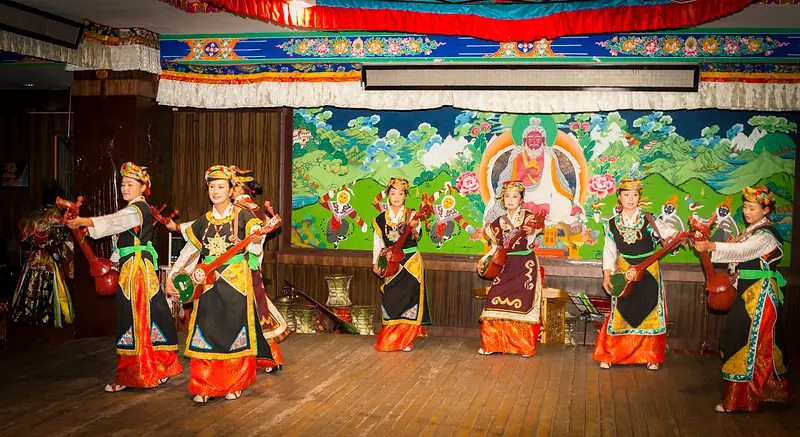 Tibetan performers in traditional costumes playing musical instruments on stage,
